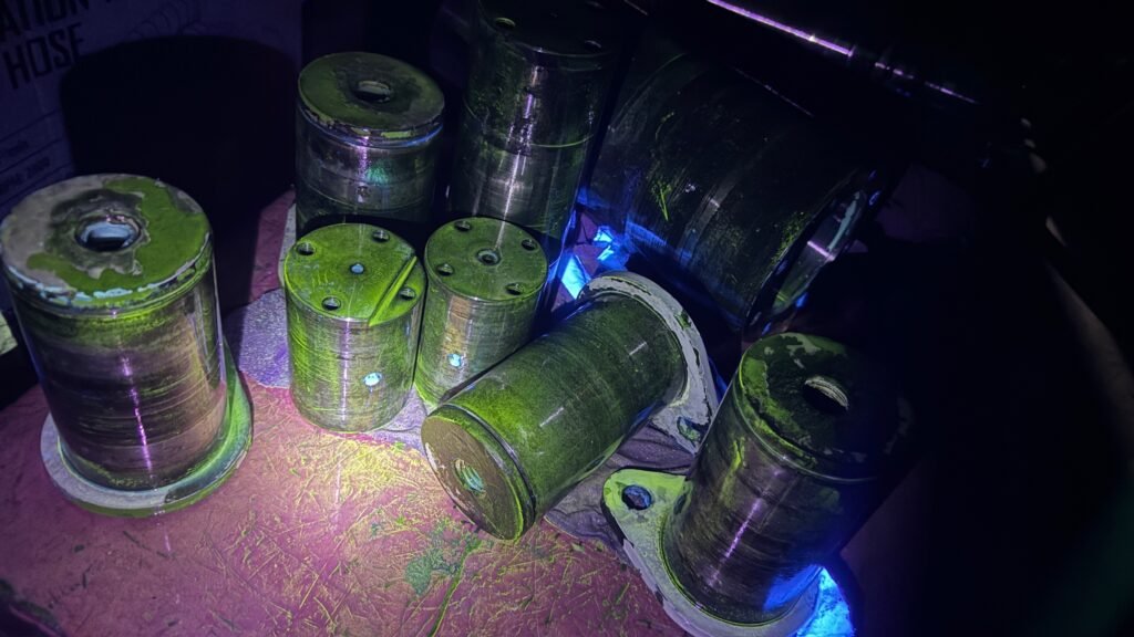 Fluorescent Magnetic Particle Testing on crane boom pins during 10 Yearly Boom Inspection showing bright green indications under UV light for crack detection